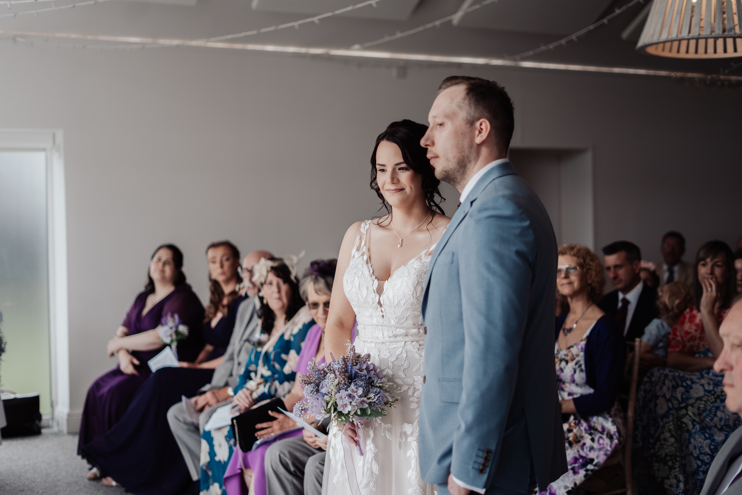 A candid shot of the bride and groom at the altar during their wedding ceremony. They are holding hands, with the groom 
                        looking forward and the bride looking slightly away.