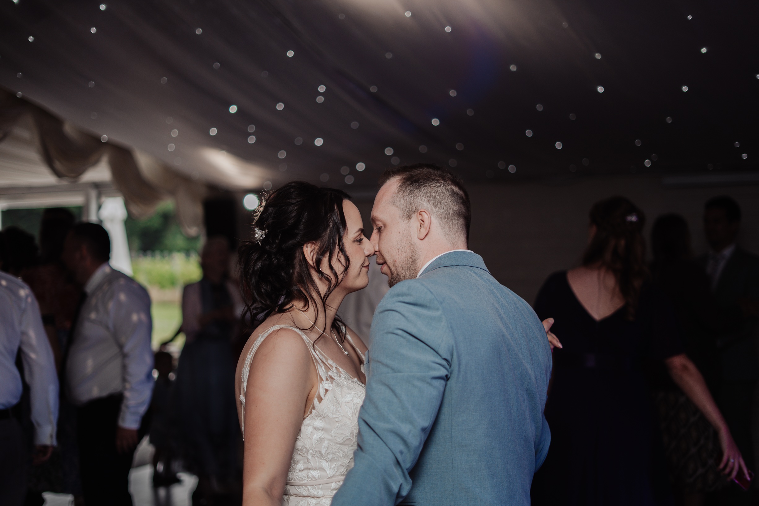 The newly married bride and groom share a moment during their first dance. They are nose to nose, with lights sparkling 
                        from the ceiling behind them at their Llanerch Vineyard reception.