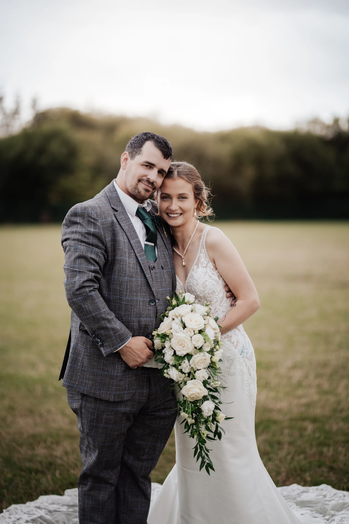 Bride in a white wedding dress and groom in a grey suit embracing in a field in Taunton.