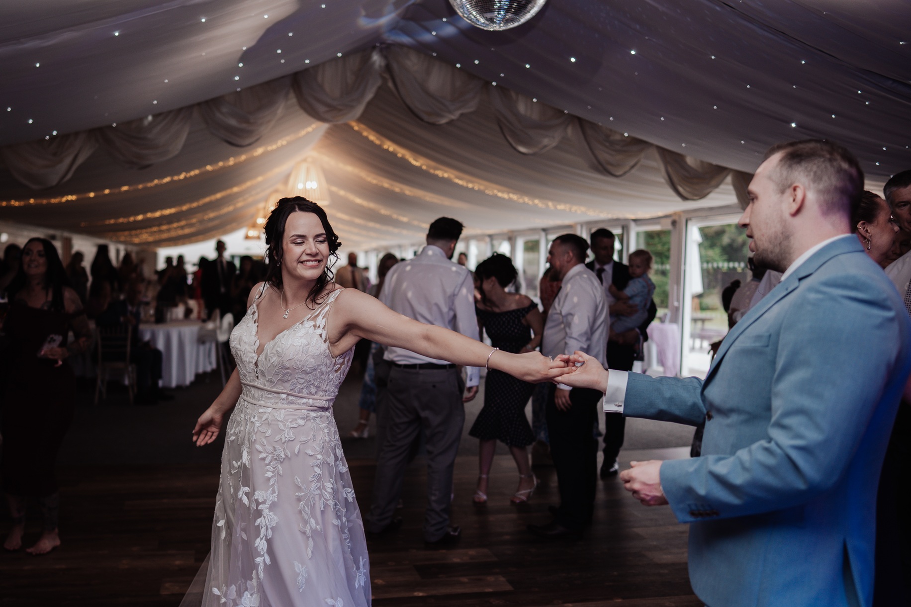 The bride and groom dance together during their reception at Llanerch Vineyard. The bride's skirt flows as she spins, 
                        and the room is decorated with a white-draped ceiling and fairy lights.